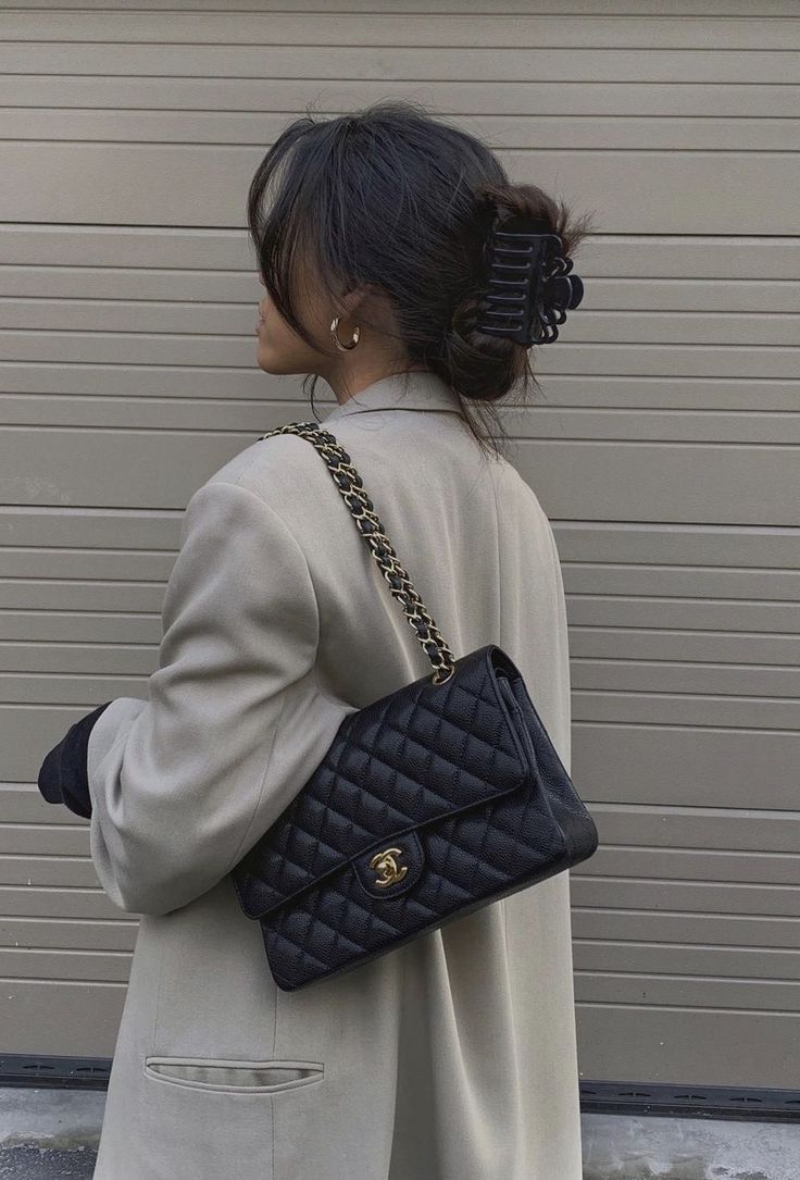 a woman carrying a black quilted handbag in front of a garage door with her back to the camera