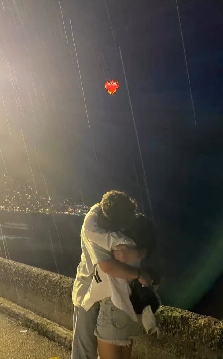 two people embracing each other while standing on the side of a road at night with kites in the sky