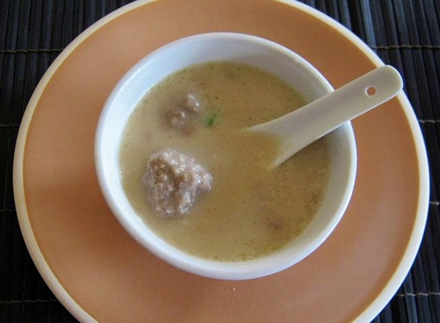 a bowl of soup with meatballs in it and a spoon on the plate next to it