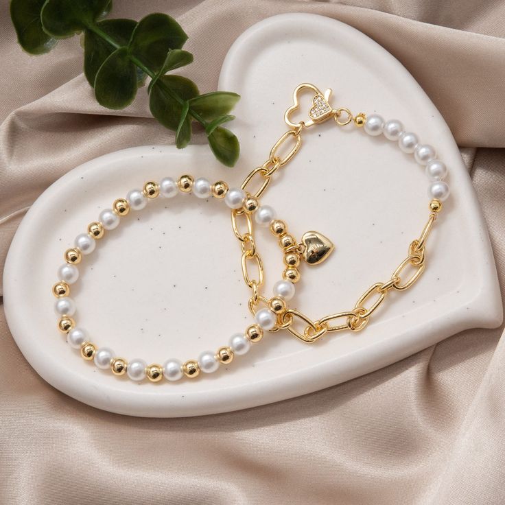 Embrace elegance and timeless charm with our enchanting "Golden Hearts Embrace" bracelet, crafted with synthetic pearls and accented with lustrous gold-filled chains, all secured by a delicate heart-shaped with rhinestones clasp. Each synthetic pearl is a symbol of purity and sophistication, exuding a classic beauty that transcends trends and time. Their smooth, iridescent surfaces shimmer delicately in the light, adding a touch of refinement to any ensemble. Interwoven among the pearls are glea Gold Heart Beads Bracelet For Party, Gold Metal Charm Bracelet With Heart Beads, Elegant Pearl Bracelet With Heart Beads For Wedding, Gold Beaded Bracelets With Heart Beads For Party, Elegant Pearl Heart Bracelet With Heart Beads, Elegant Metal Beaded Bracelet With Heart Charm, Gold Pearl Jewelry With Heart Charm, Gold Party Beaded Bracelets With Heart Beads, Elegant Beaded Bracelet With Heart Charm For Valentine's Day