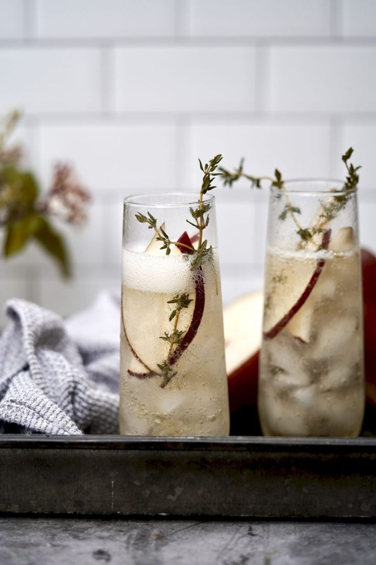 two glasses filled with liquid sitting on top of a metal tray next to an apple