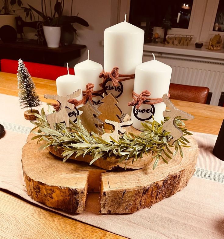 a wooden table topped with candles and greenery next to a christmas tree branch on top of a piece of wood