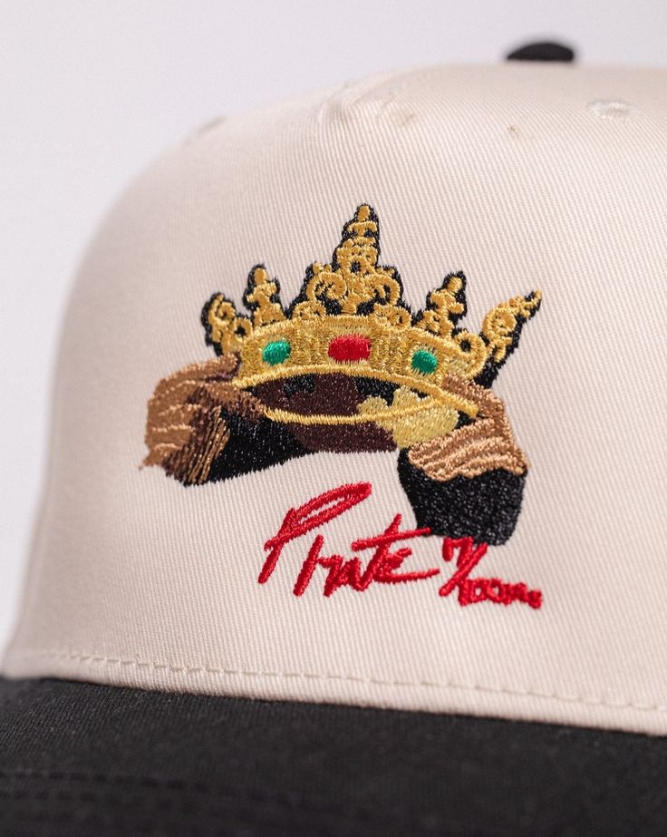 Pirate Castles Crown Hat Size: Adjustable Snapback Cap Color: Cream/Black Front Pirate Castles Crown Design Embroidery Stitch Count: 5,398 Embroidery Color: Gold, Red, Emerald Green, Brown, Black Embroidered Cream Cap, Cream Embroidered Cap, Embroidered Snapback Hat, Embroidered Flat Brim Baseball Cap, Hat Cream, Crown Hat, Embroidery Stitch, Crown Design, Design Embroidery