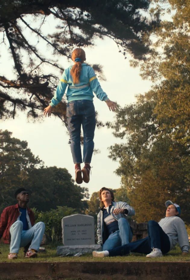 three people are sitting on the ground in front of a tree and one person is jumping up into the air