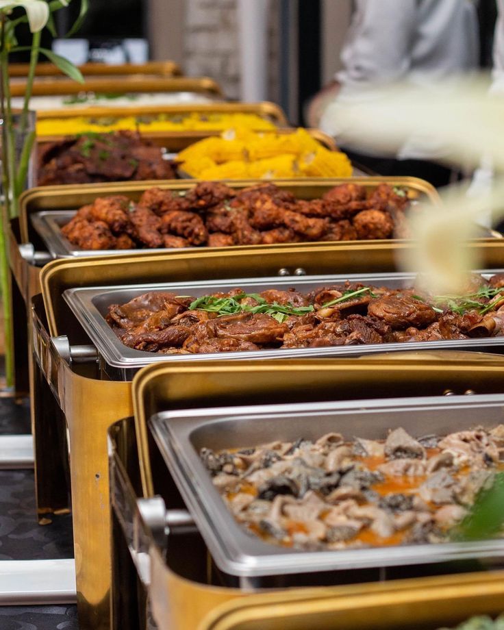 several trays of food are lined up on a table with flowers in the background