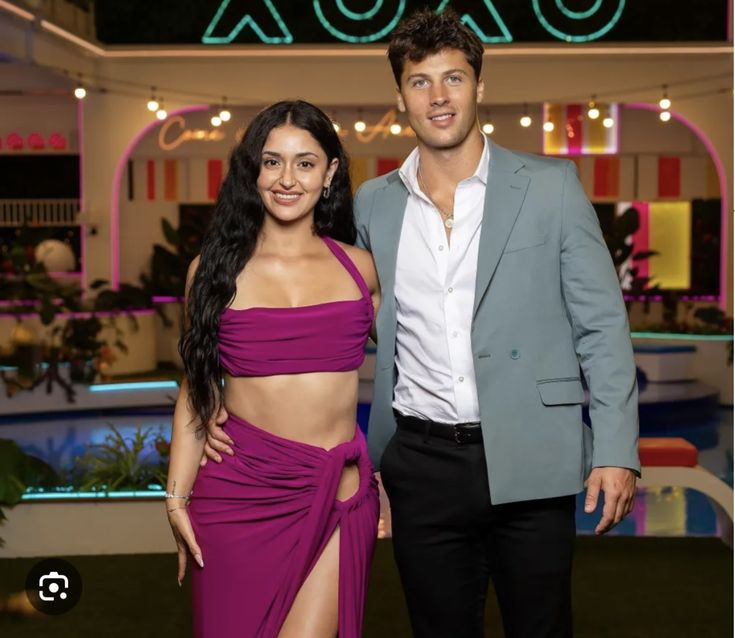 a man and woman standing next to each other in front of a building with neon lights