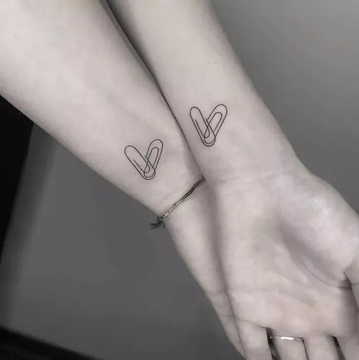 two people with matching tattoos on their arms, one holding the other's hand