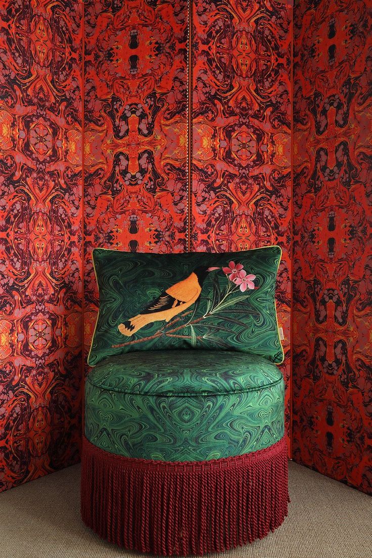 a green chair sitting in front of a red wall covered in intricately designed wallpaper