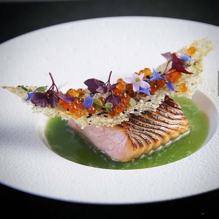 a white plate topped with meat covered in vegetables and garnished with edible flowers