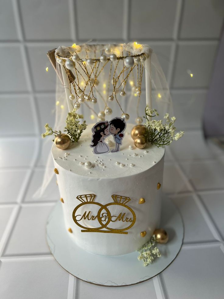 a white wedding cake with gold decorations and lights on the top, sitting on a tile floor