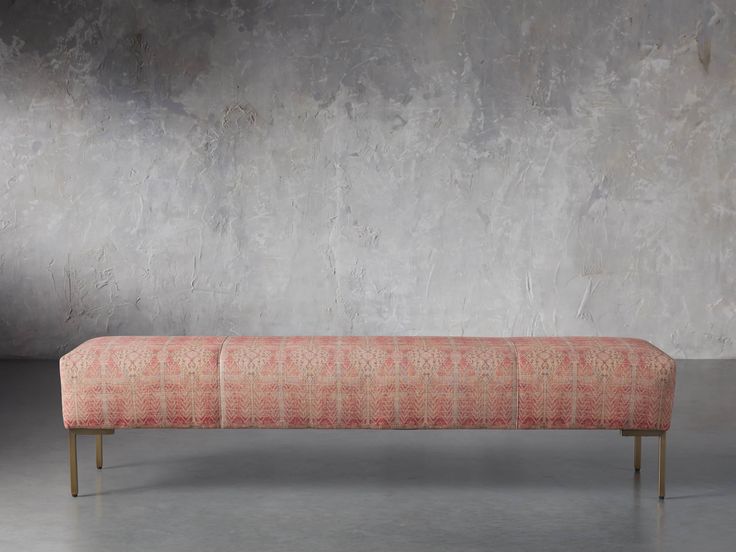 an orange bench sitting in front of a gray wall and cement floor with no one on it