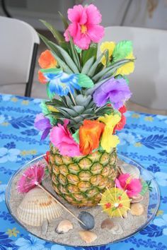 a pineapple decorated with colorful flowers on a blue table cloth next to shells and seashells