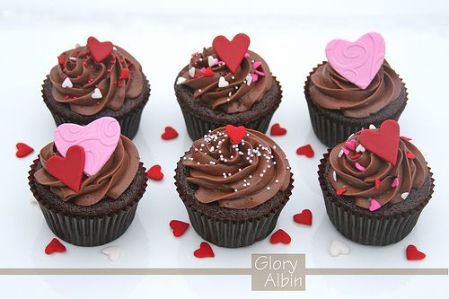 chocolate cupcakes decorated with hearts and sprinkles on a white surface