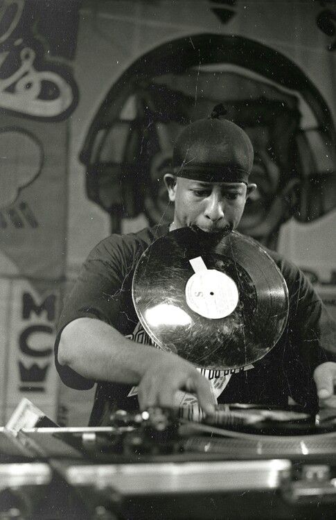 a man holding a record player in his right hand and wearing a hat on top of it