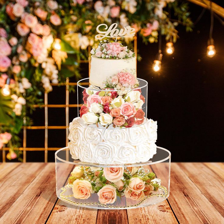 three tiered wedding cake with pink and white flowers on the top, sitting on a wooden table