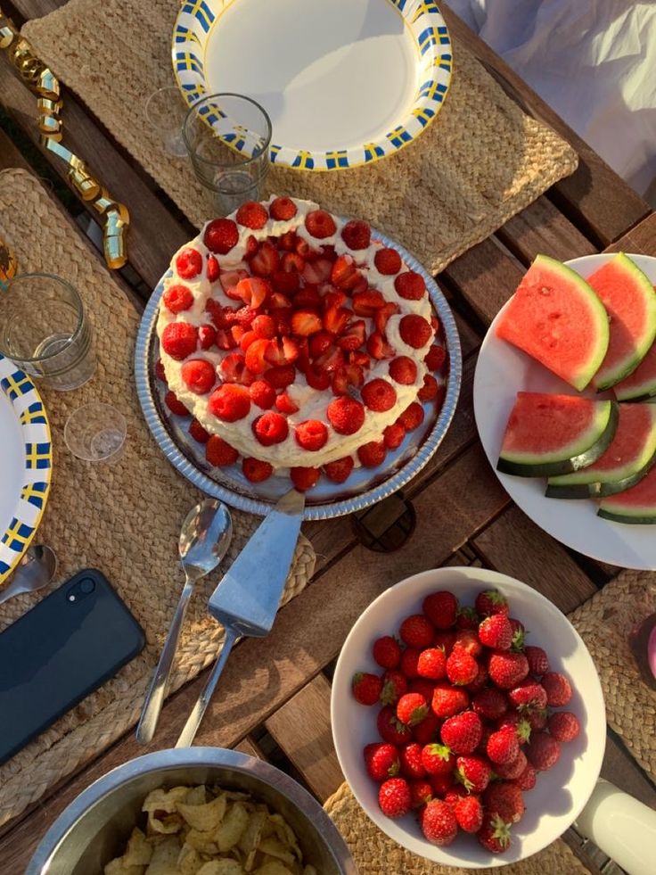 there is a cake with strawberries on it and watermelon slices in bowls