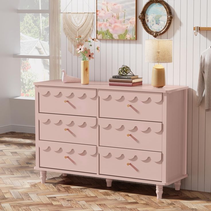 a pink dresser with drawers and pictures on the wall