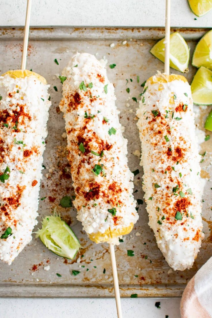 three fish skewers on a baking sheet with limes and seasoning next to them