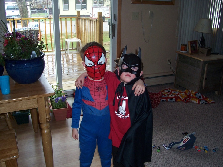 two young boys dressed up as spider - man and batman, standing next to each other