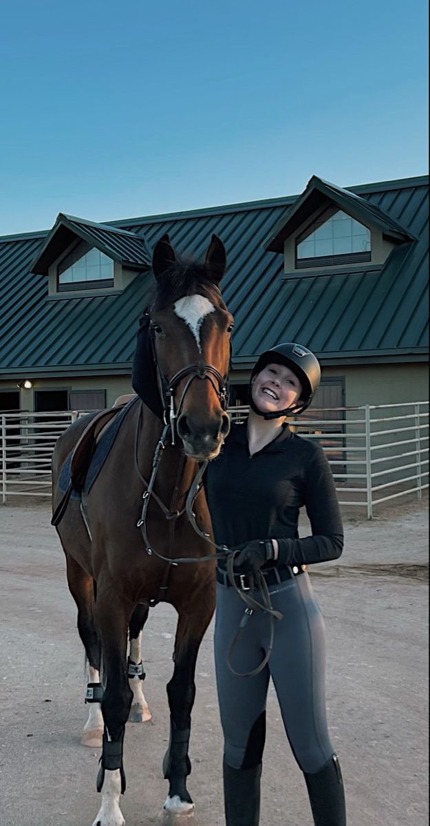 a woman standing next to a brown horse in front of a building with a black roof