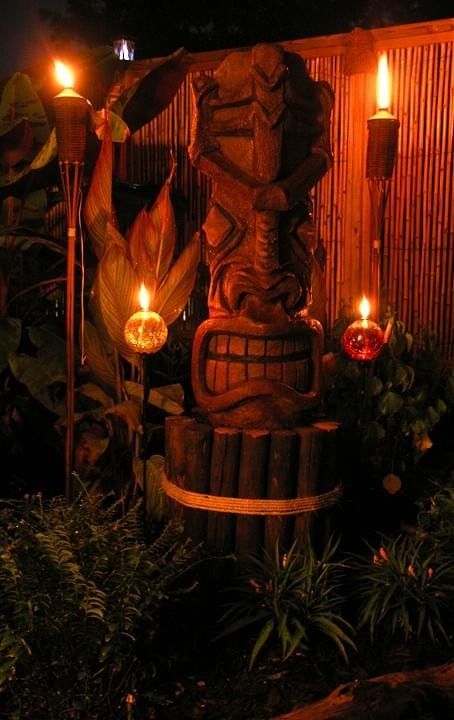 a tiki statue in the middle of some plants and candles lit up at night