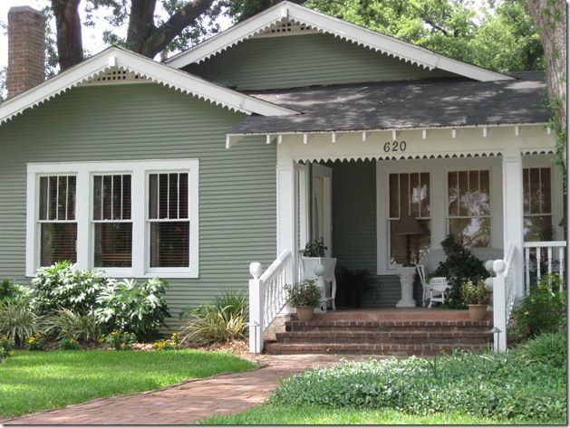 a green house with white trim on the front porch and steps leading up to it