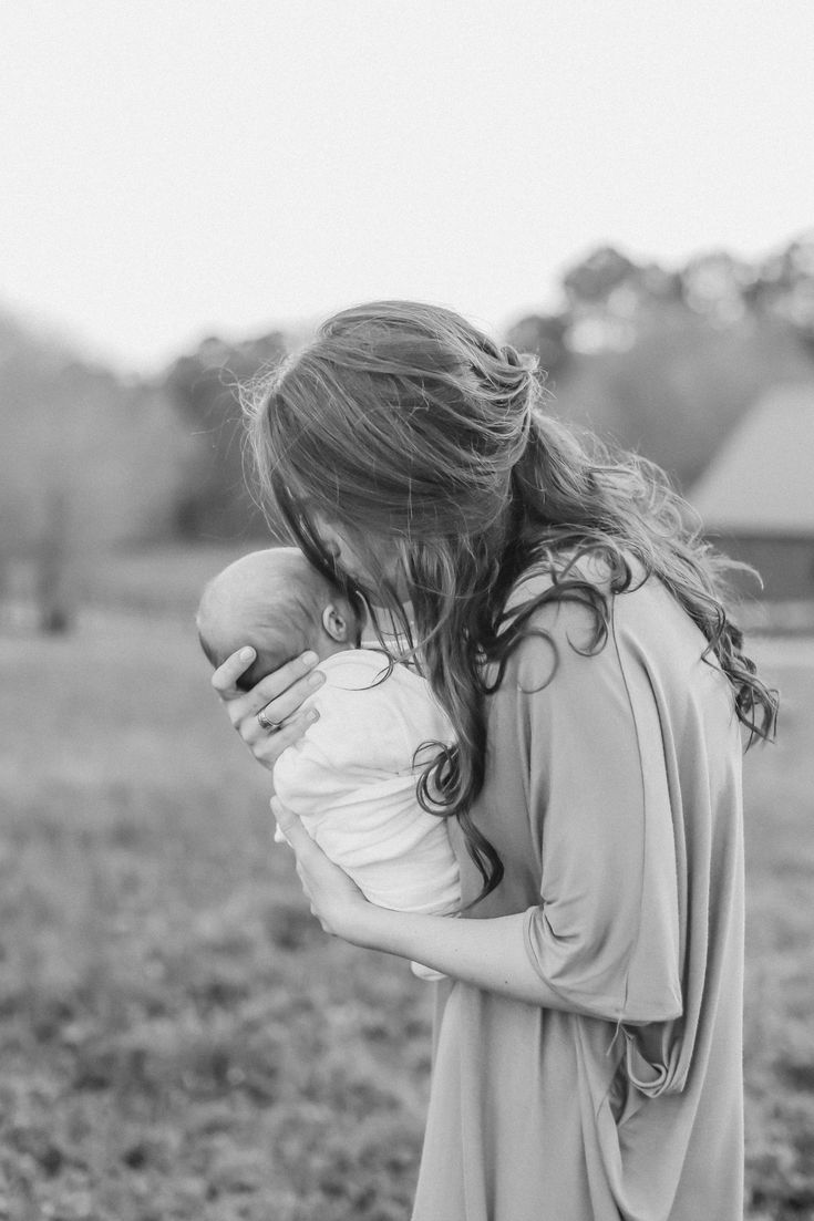 a woman holding a baby in her arms while standing on top of a grass covered field