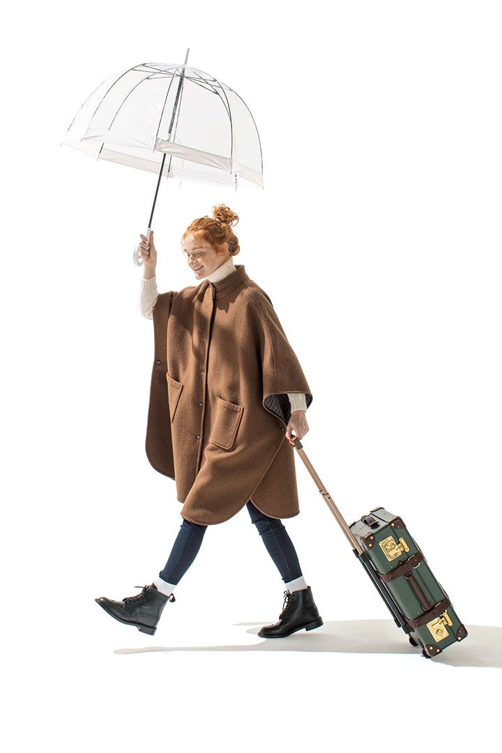 a woman walking while holding an umbrella over her head and carrying luggage behind her back