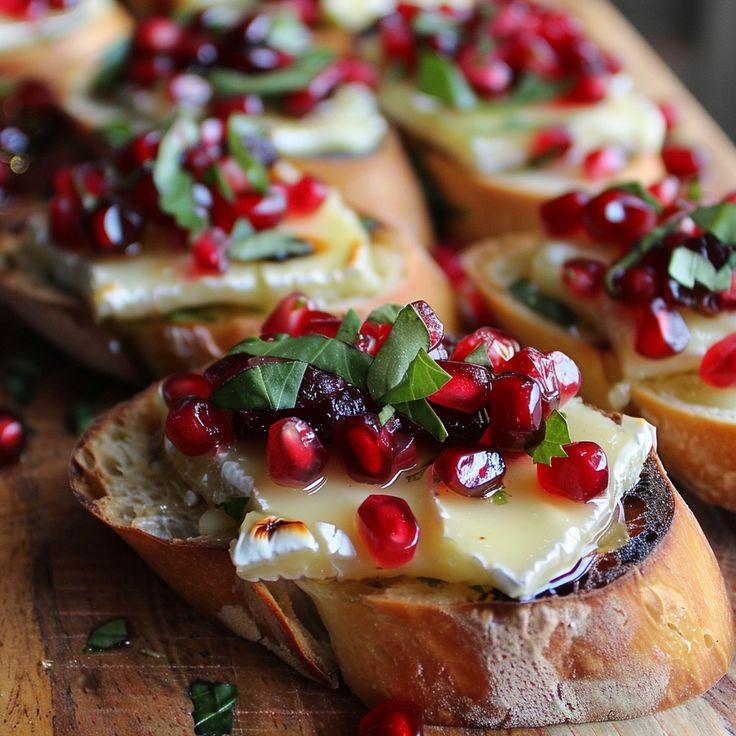 crostini with cheese, pomegranate and herbs on top sitting on a wooden cutting board