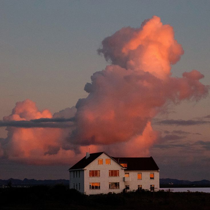 a white house sitting on top of a lush green field under a pink cloud filled sky