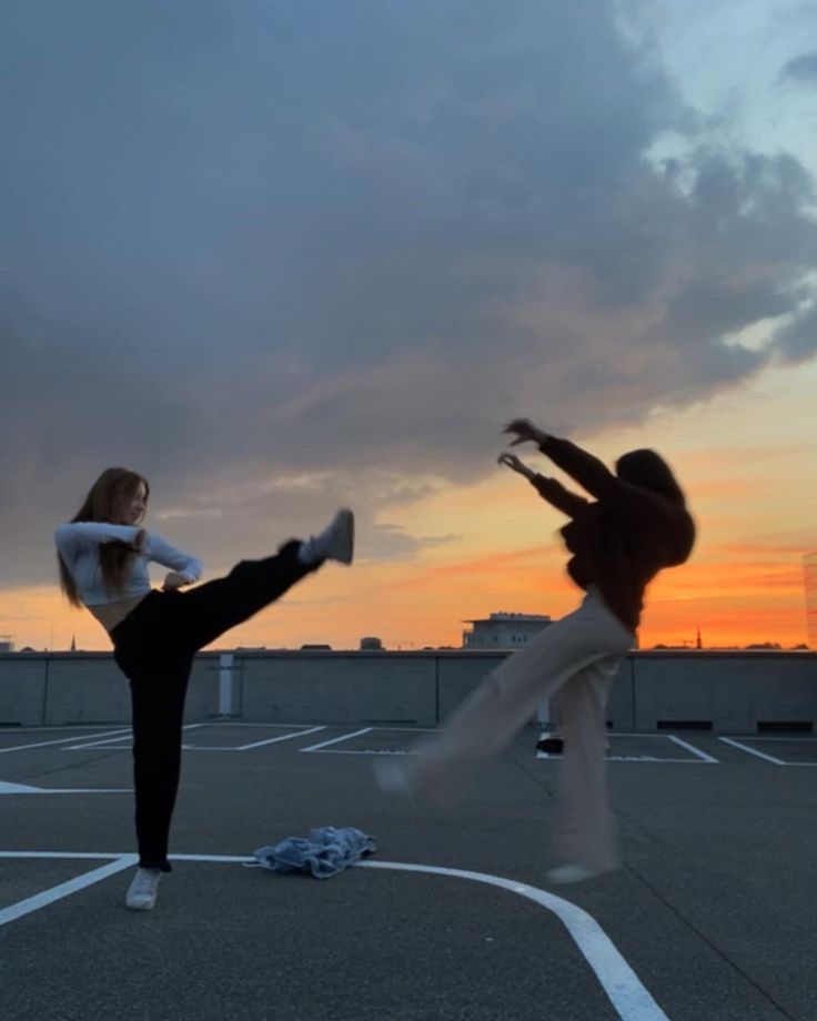 two people are doing tricks in an empty parking lot at sunset with the sun setting behind them