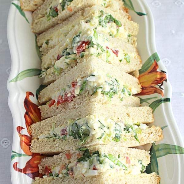 there are many sandwiches on the white platter with green and red flowers around it