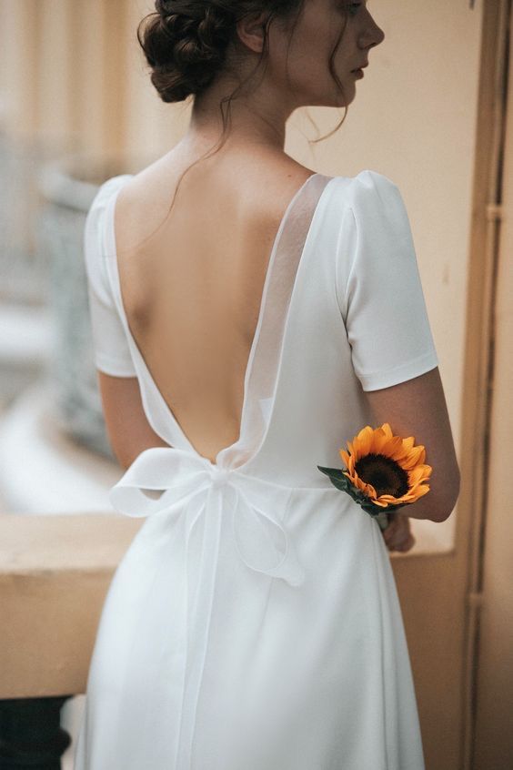 the back of a woman's dress with a sunflower in her left hand