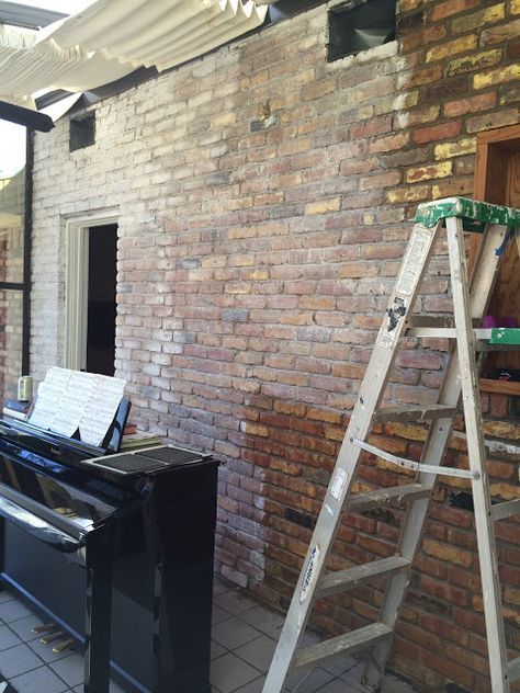 a black piano sitting in front of a brick wall next to a ladder and window