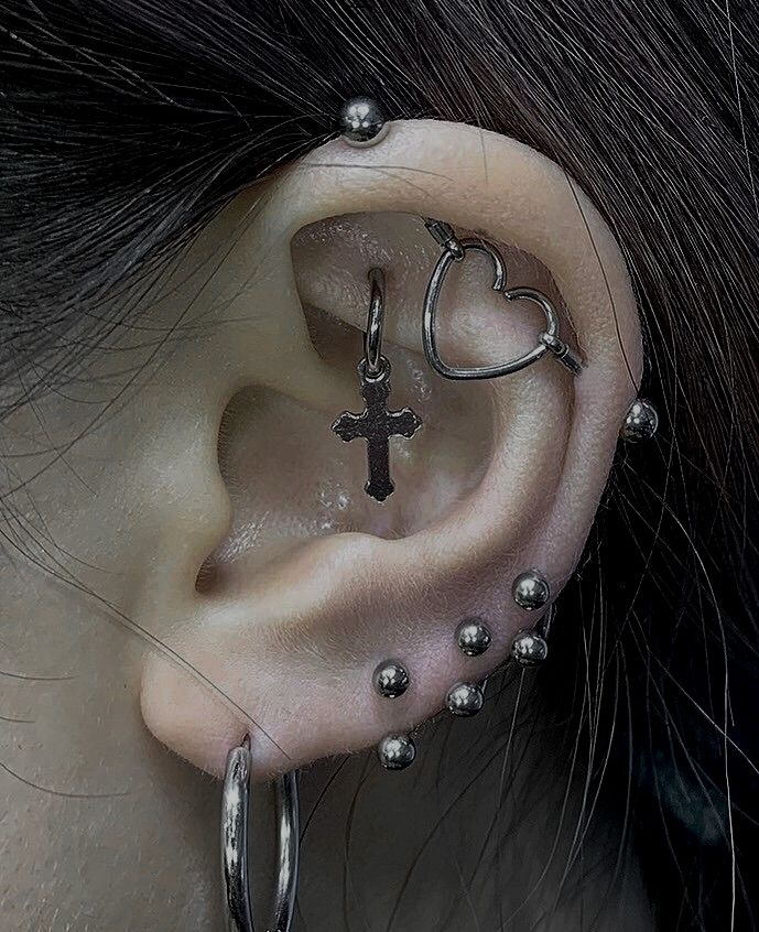 a woman with piercings on her ear wearing a cross and heart shaped hoop earrings