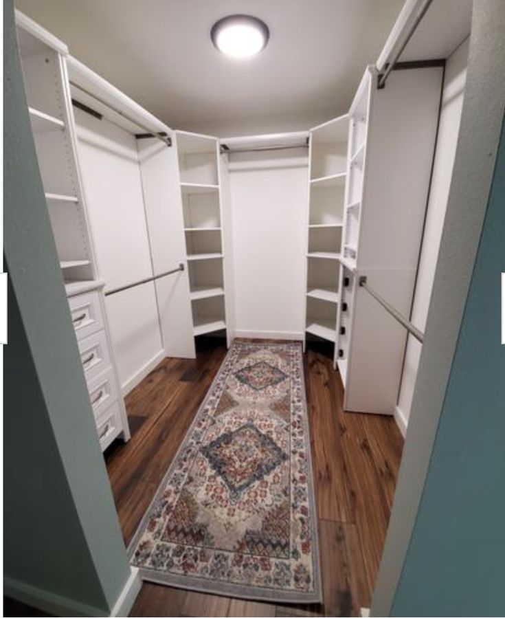 an empty walk in closet with white cabinets and rug on wooden flooring next to blue walls