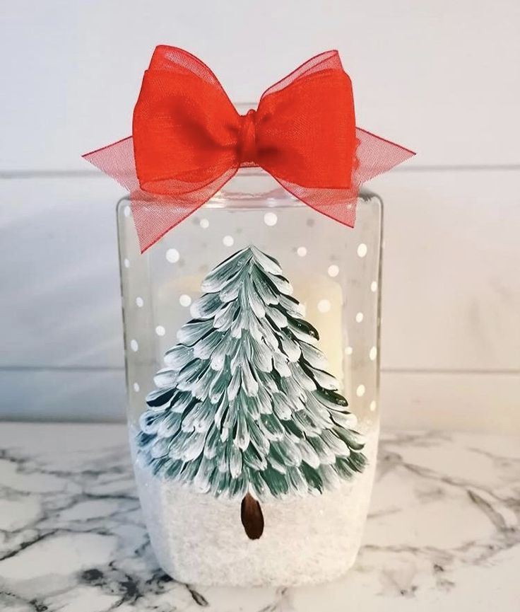 a snow globe with a christmas tree inside and a red bow on the top, sitting on a marble countertop