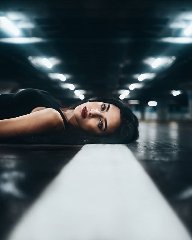 a woman laying on the ground in an underground parking garage with her head down and eyes closed