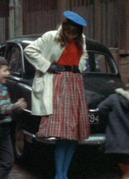 a woman standing in front of a black car with a blue hat on her head