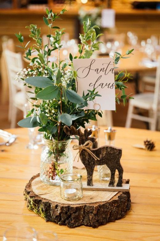 a wooden table topped with vases filled with flowers and greenery next to a sign