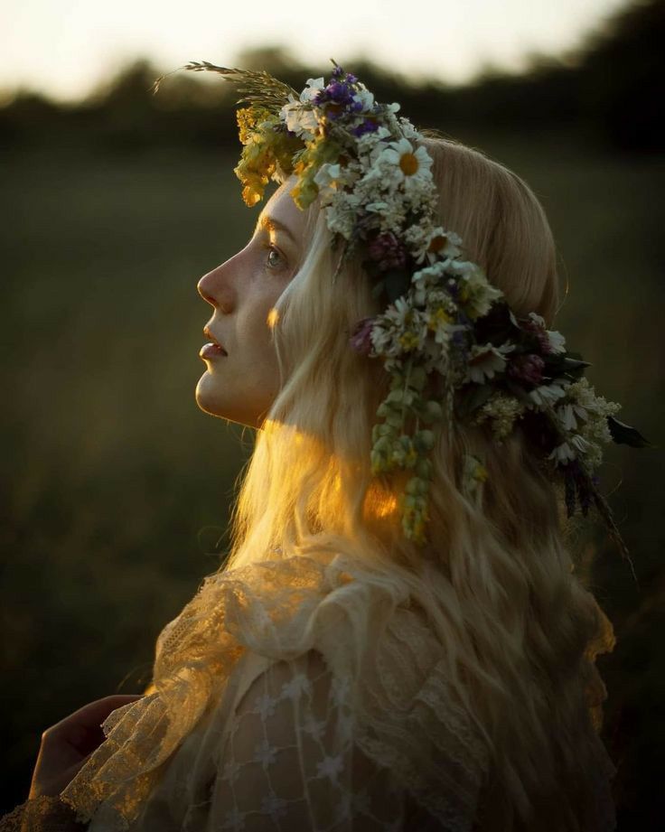 a woman with long blonde hair wearing a flower crown on her head and looking off into the distance