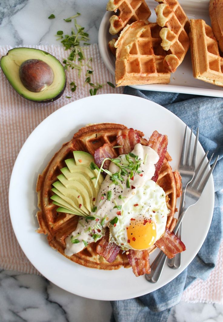 a waffle topped with bacon, avocado and an egg on a plate