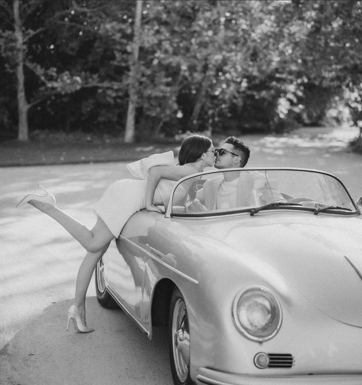 a man and woman kissing in front of a convertible car