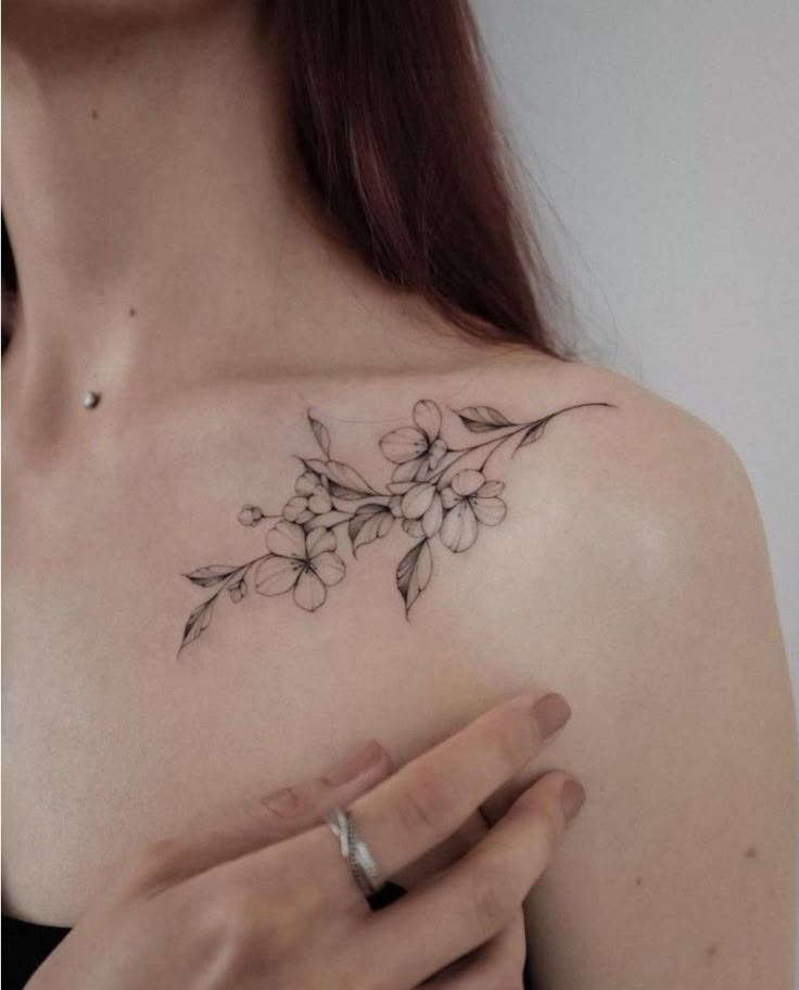 a woman's shoulder with flowers on it and a ring in her left hand