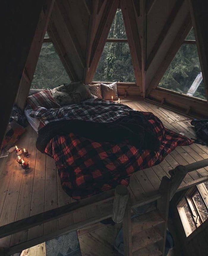 a bed in the middle of a room with wooden flooring and windows above it