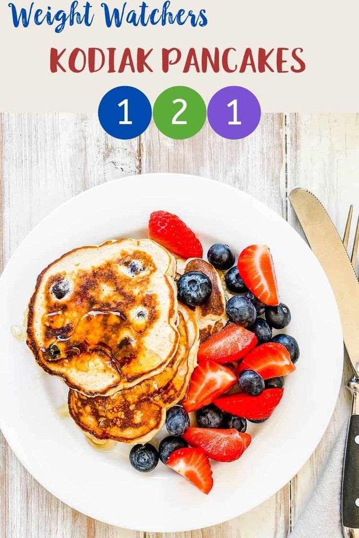 a white plate topped with pancakes covered in berries and blueberries next to a knife and fork