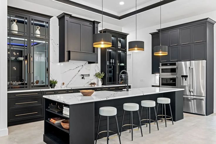 a kitchen with black cabinets and white counter tops, gold pendant lights over the island