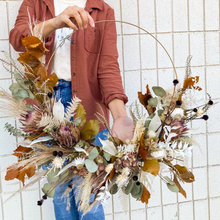 a woman holding a floral arrangement in front of a white brick wall with her hands