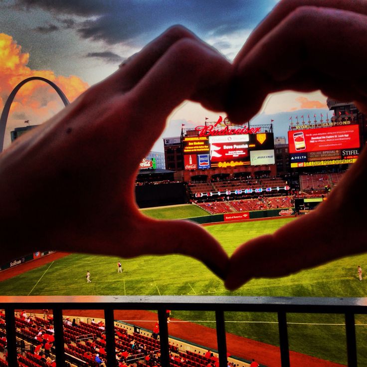 two hands making a heart shape in front of a baseball field and the st louis arch