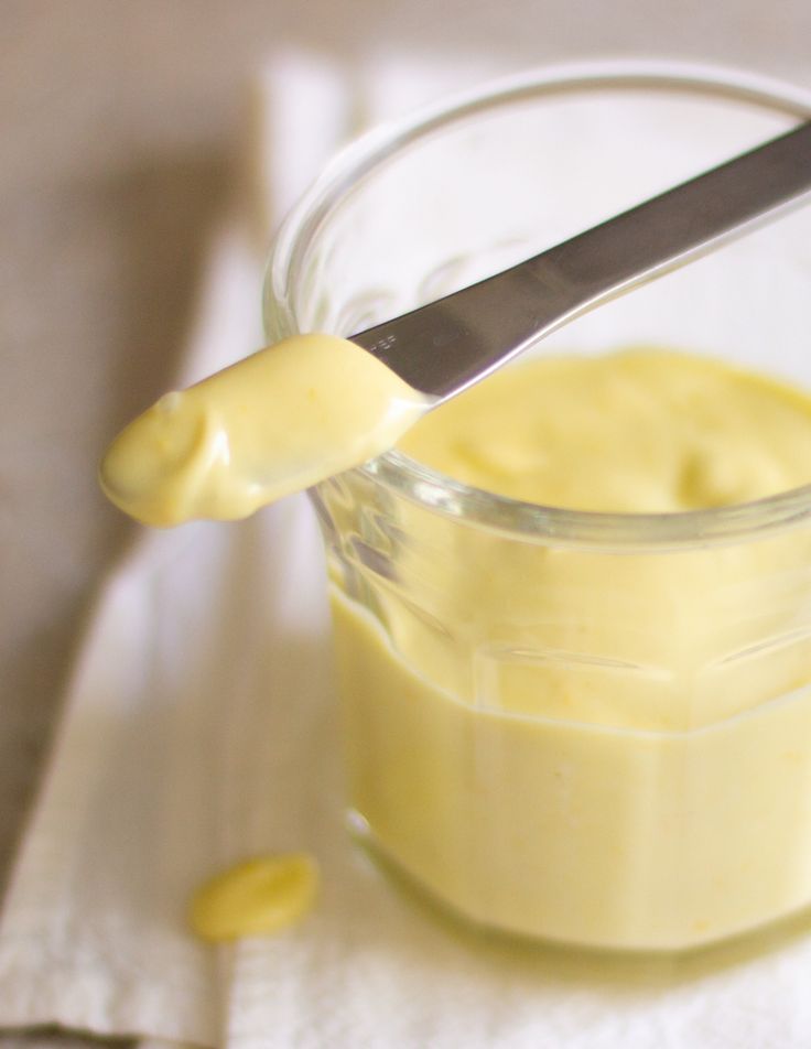 a glass jar filled with yellow liquid sitting on top of a wooden table next to a spoon